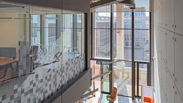 A top view of workinton space, part of a glass office on the left, and a part of the open meeting space on the right.