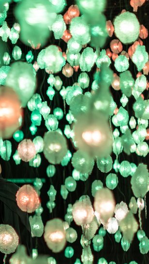 Two people looking at artwork by Pipilotti Rist of hanging lights in green and orange.