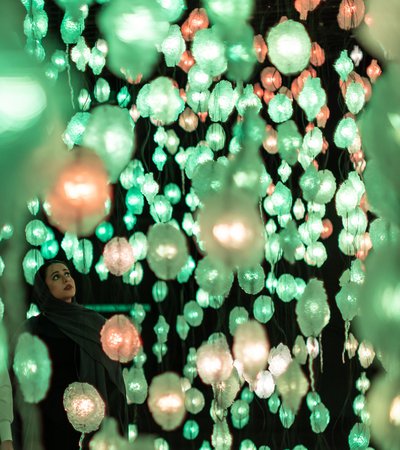 Two people looking at artwork by Pipilotti Rist of hanging lights in green and orange.