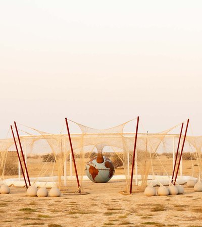 Installation made of a white crocheted net that shows octagonal structure with a sculpture of the earth placed in the center