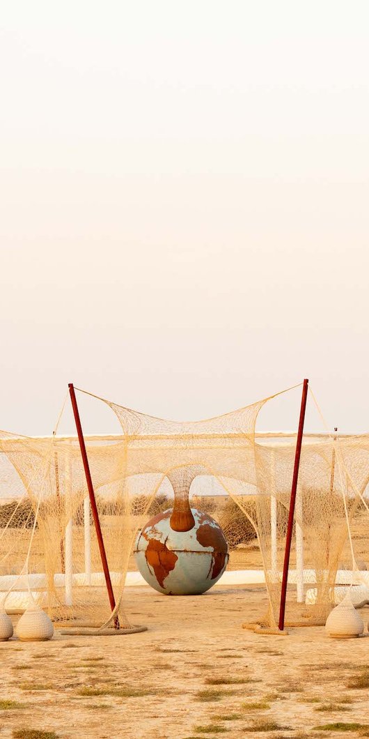 Installation made of a white crocheted net that shows octagonal structure with a sculpture of the earth placed in the center