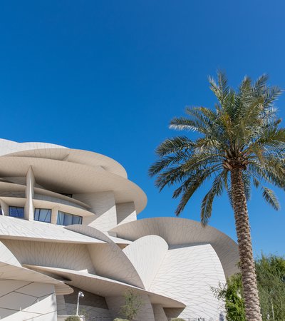 An exterior shot of the National Museum of Qatar and one of the surrounding palm trees