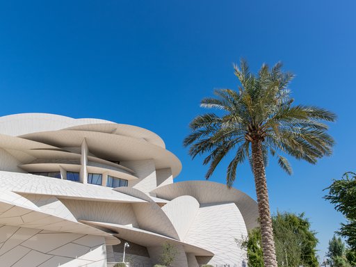 An exterior shot of the National Museum of Qatar and one of the surrounding palm trees