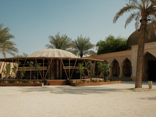 A tent-like structure with bamboo poles holding the perimeter sits in the middle of a courtyard flanked by palm trees.