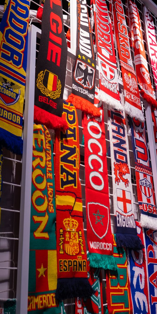 Photo of multiple, colourful football scarves hanging on a white, caged, frame.