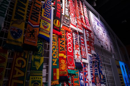 Photo of multiple, colourful football scarves hanging on a white, caged, frame.