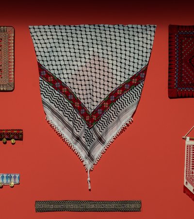 Different embroidered textiles hang against a red wall.