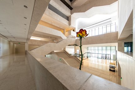 A two-story tall metal sculpture of a rose with red and white petals inside the entrance to the M7 building.