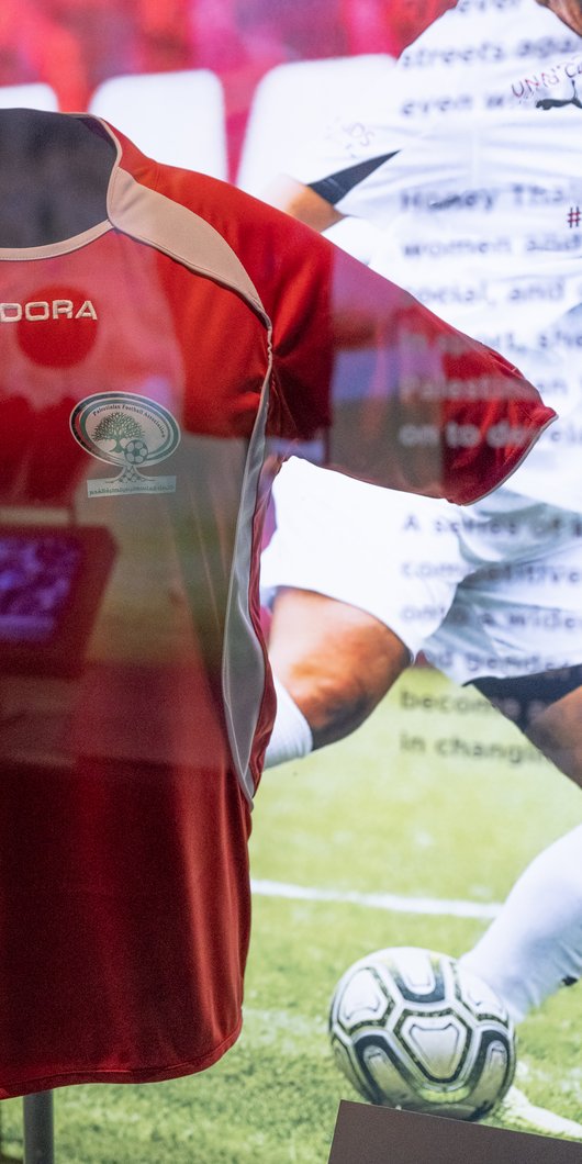 Red Palestinian Football Association shirt on display behind glass case.