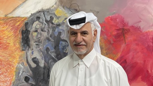 Ruwad Artist Hassan Al-Mulla standing next to his paintings in his studio at the Fire Station.