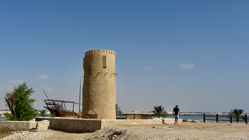 The Al Kor stone tower seen within the wider landscape with a man walking beside it