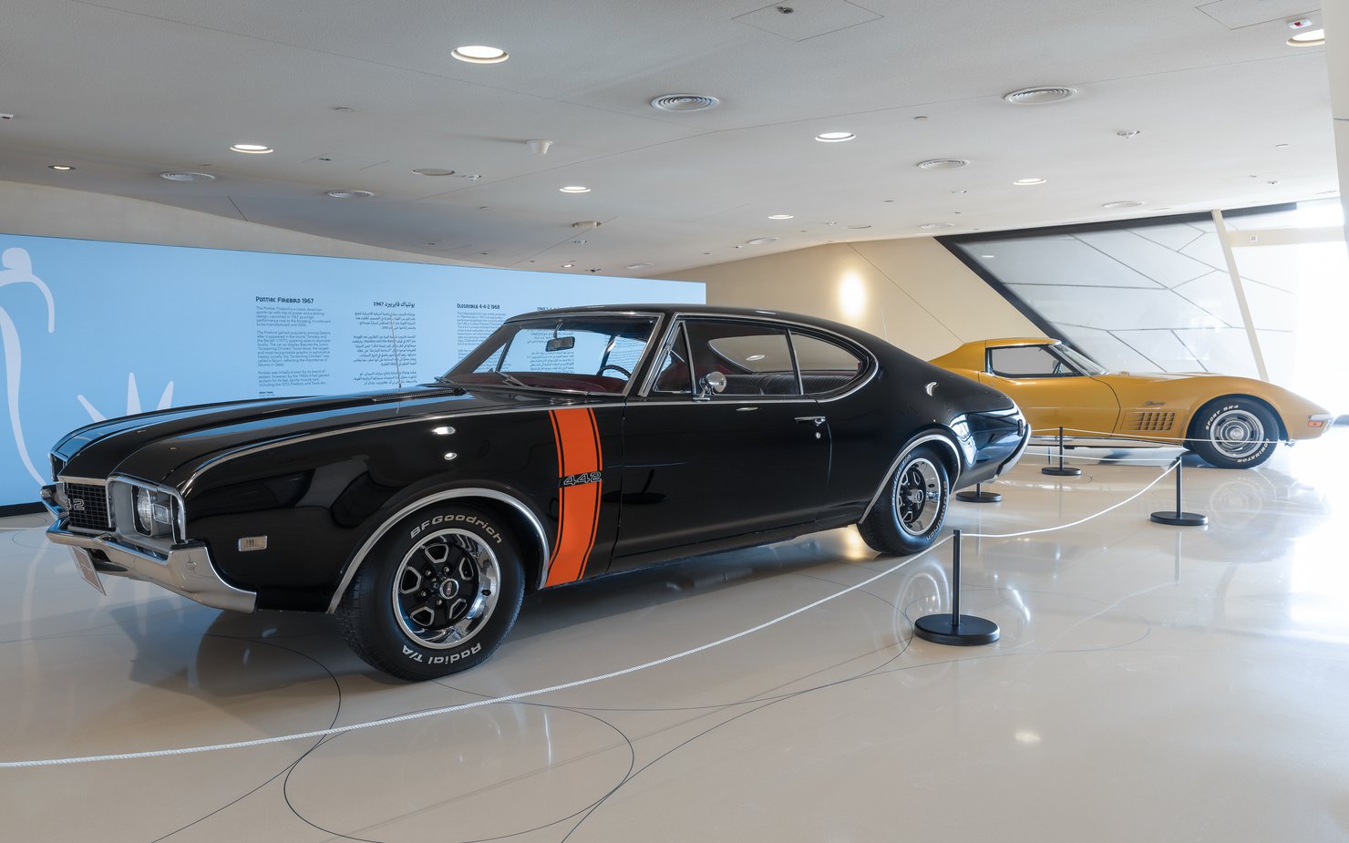 Two vintage American cars, one black and one yellow, parked in the Mawater Gallery, NMoQ