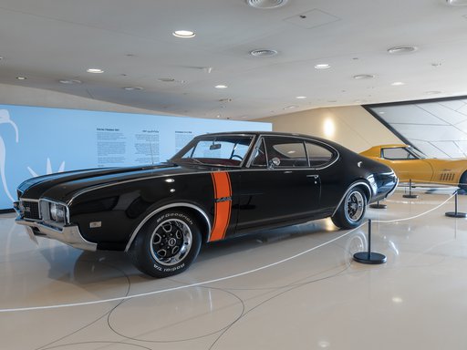 Two vintage American cars, one black and one yellow, parked in the Mawater Gallery, NMoQ