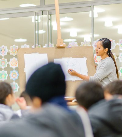 Teacher showing the children how to draw a flower on a board