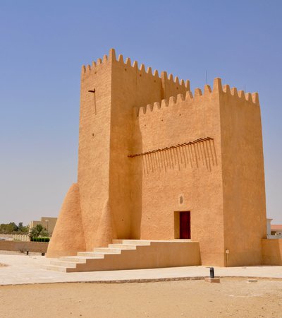 A tall angular tower made from sand coloured material with an open doorway and crenellations around the top of the building