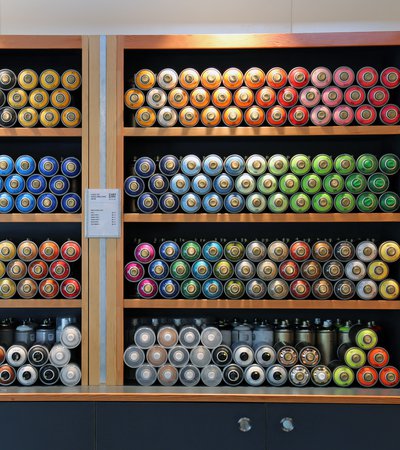 Interior of an artist supply shop with shelving, graphic signage and a rear wall displaying multiple rows of acrylic tubes of paint