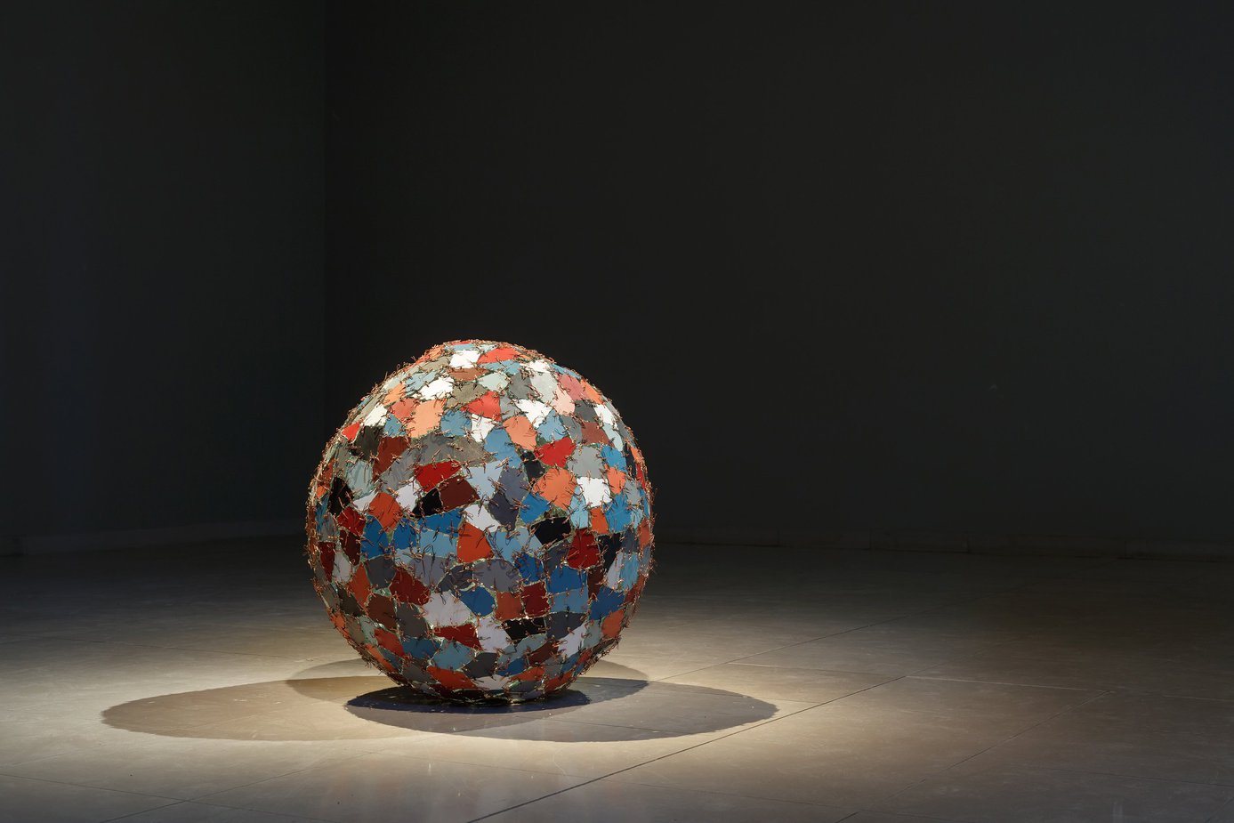 A spotlight on the object Chaos+Repair=Universe showcasing a sculpture with coloured mirror fragments stitched into a ball shape with metal wires