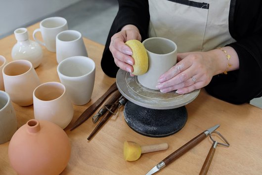 Close view of a woman making a pot in clay on a pottery wheel.