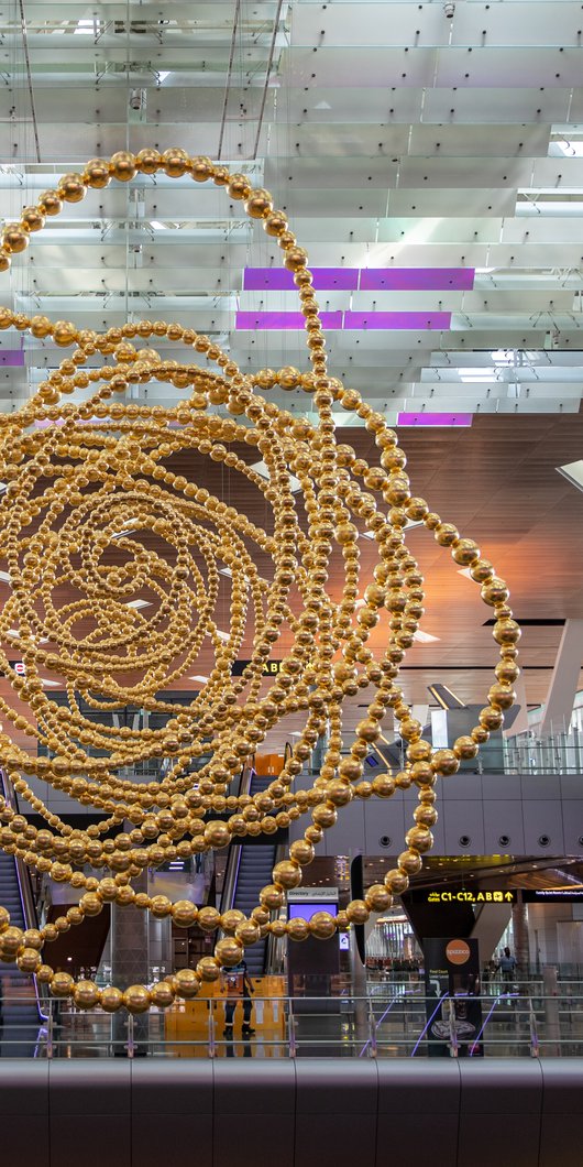 A large golden sculpture 'Cosmos' constructed of many concentric circular shapes suspended from the ceiling within an airport terminal