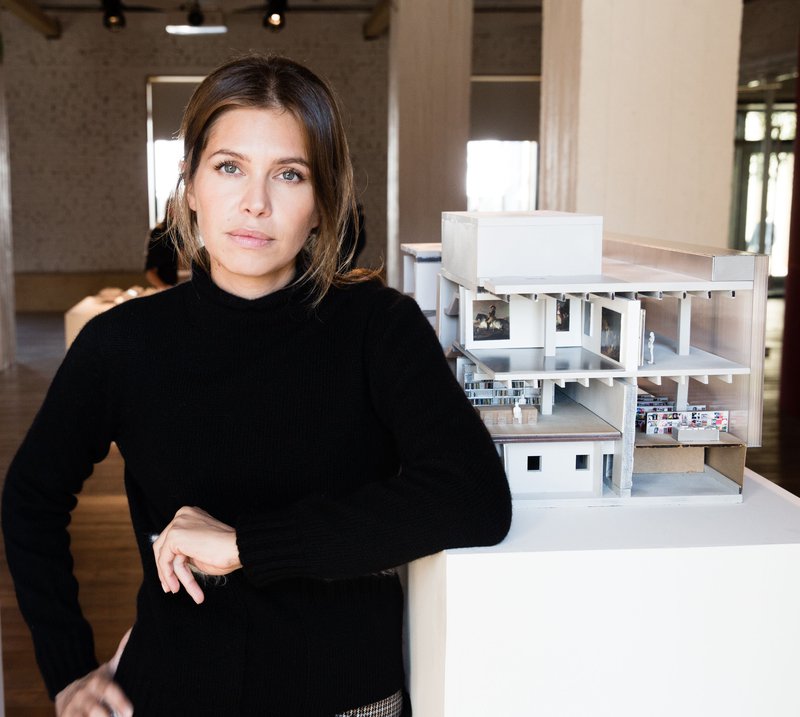 Portrait of Dasha Zhukova leaning against a table featuring an architectural model