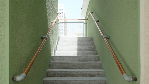 Outdoor staircase with wooden handles and green wall.