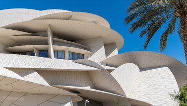 Decorated stone arches with a doorway in shade and a view of the National Museum of Qatar in the background