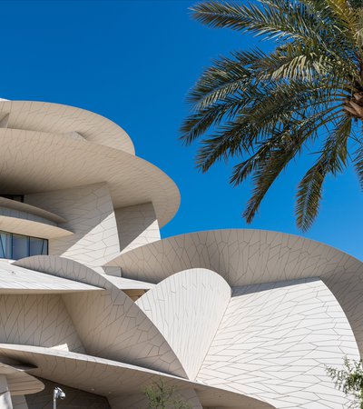 Decorated stone arches with a doorway in shade and a view of the National Museum of Qatar in the background