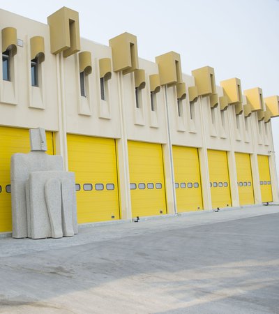 Exterior of The Fire Station Artist in Residence building showing its bright yellow shutter doors and sculpture at the entrance