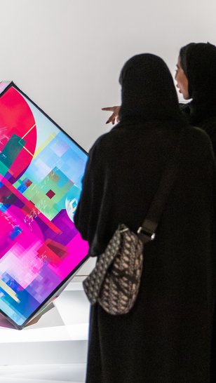 Two ladies in abaya viewing and pointing towards a digital artwork at the fire station gallery