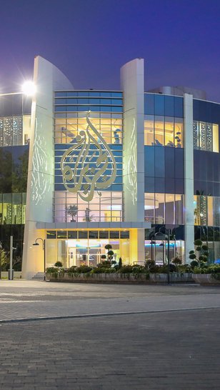 The outside of a building with the Al Jazeera logo mounted on the front.