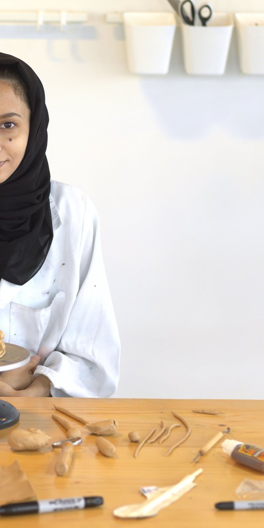 Hana Al Saadi sitting in a workshop surrounded by fresh clay objects