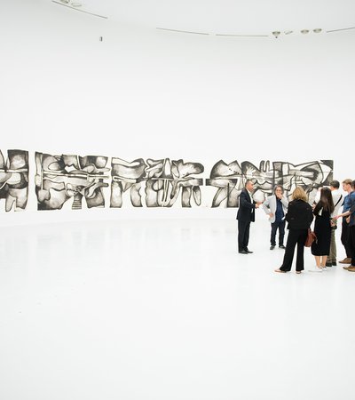 A group of visitors at the Al Riwaq's gallery space with works from Dia Al Azzawi's exhibition in the background