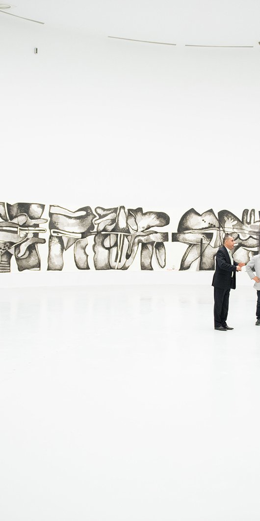 A group of visitors at the Al Riwaq's gallery space with works from Dia Al Azzawi's exhibition in the background