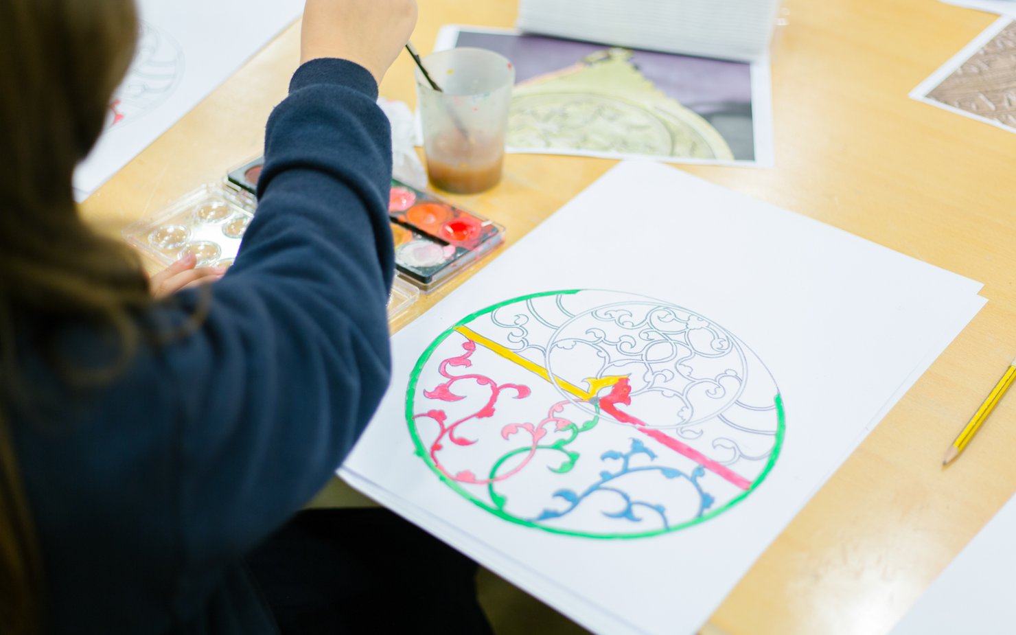 A child painting inside the lines of an Islamic design on paper