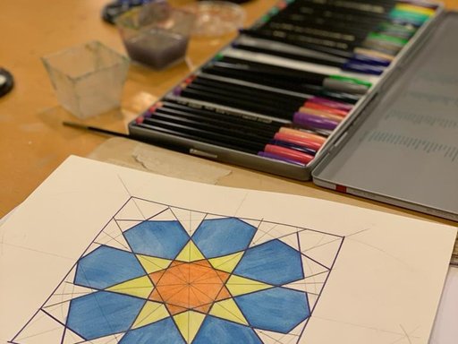 A close-up shot of a sheet of paper filled with geometric designs filled in with coloured pencils
