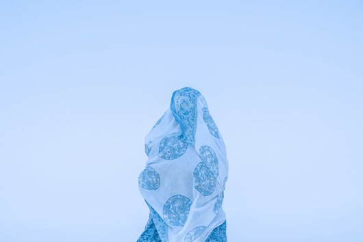 A photo of a female with white and blue fabric wrapped around them standing against a light blue background.