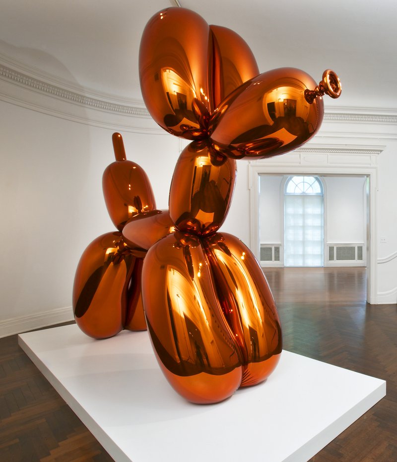 A shiny, orange metal sculpture in the shape of a dog made out of balloons