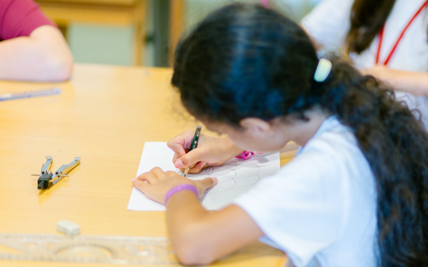 A girl sketches out geometric shapes on a white piece of paper for her kufic calligraphy