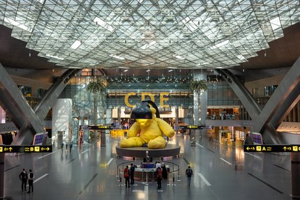 A sculpture of a  yellow teddy with a lamp above its head at Hamad International Airport