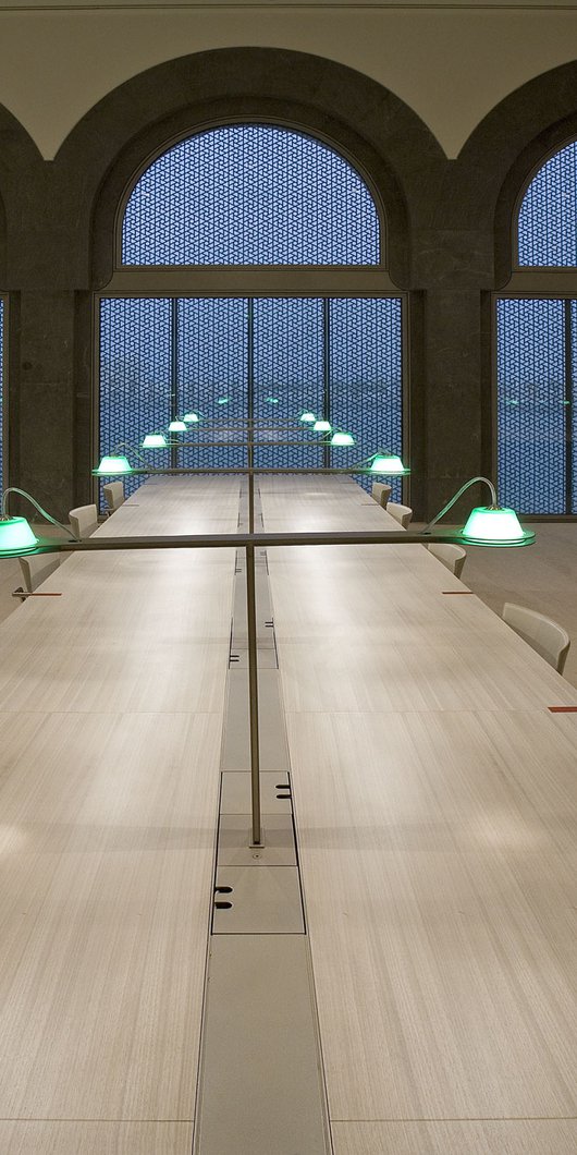 Interior view of MIA's library seating area with three very long tables stretching towards arched windows overlooking Doha city