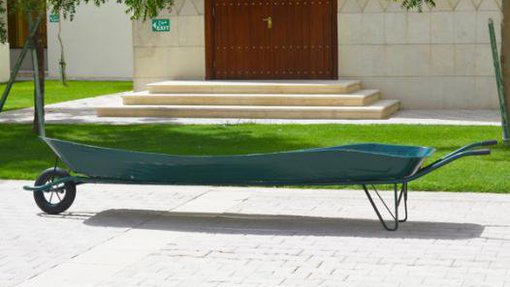 Long dark green wheelbarrow created by Hana Al Saadi standing in front of a small garden at Virginia Commonwealth University Qatar