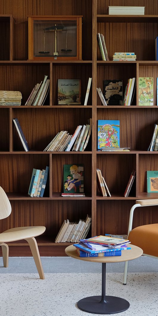 Interior view of a seating area in Liwan's library with two chairs, small table and bookshelves in the background.