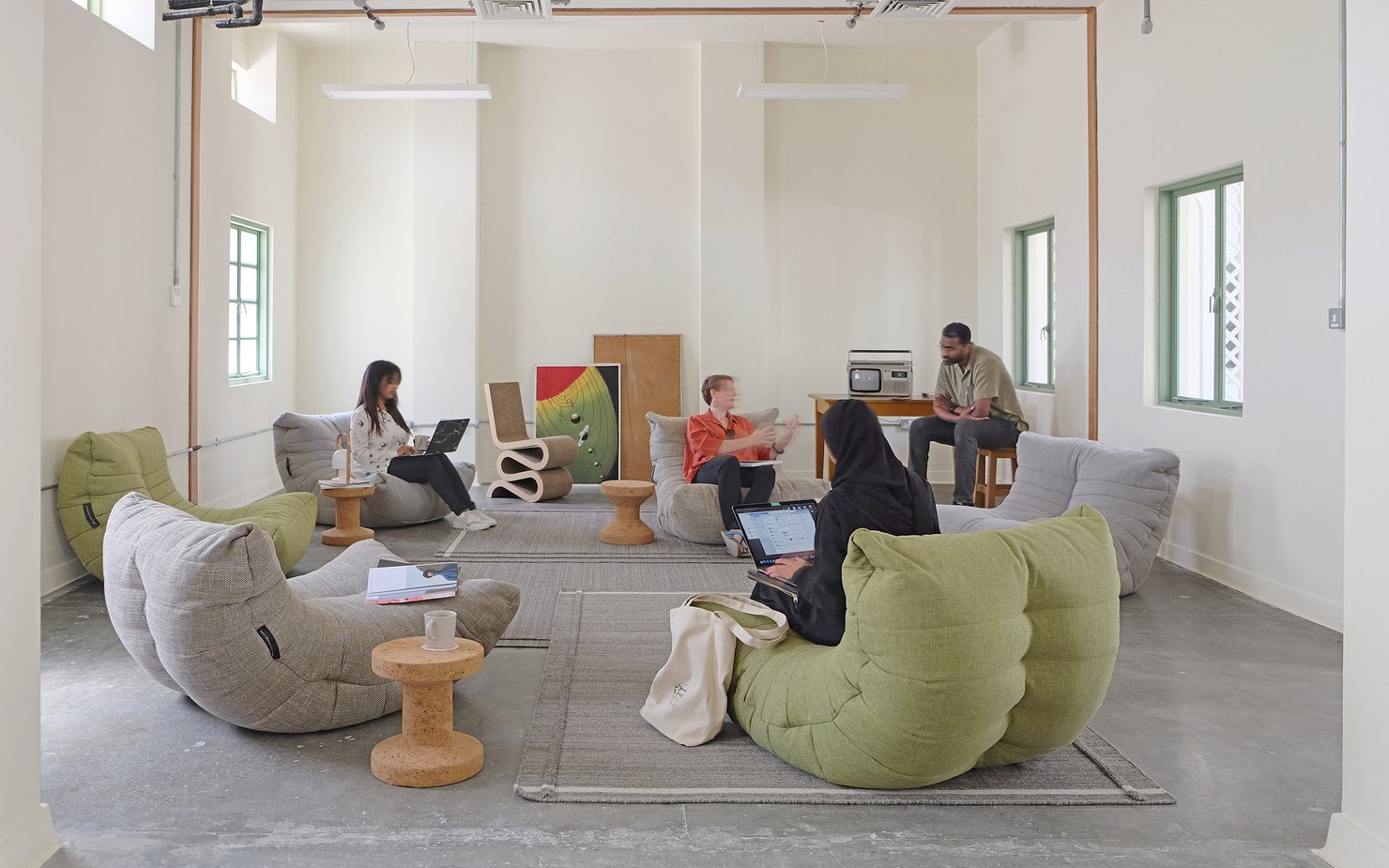 Indoor lounge area with large bean-bag style seating with people relaxing and talking.