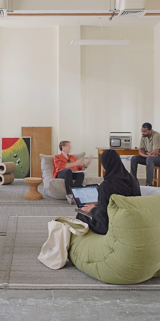 Indoor lounge area with large bean-bag style seating with people relaxing and talking.