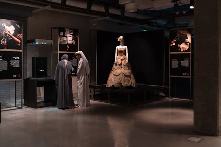 Two visitors at an exhibition with a gowned mannequin in the background.