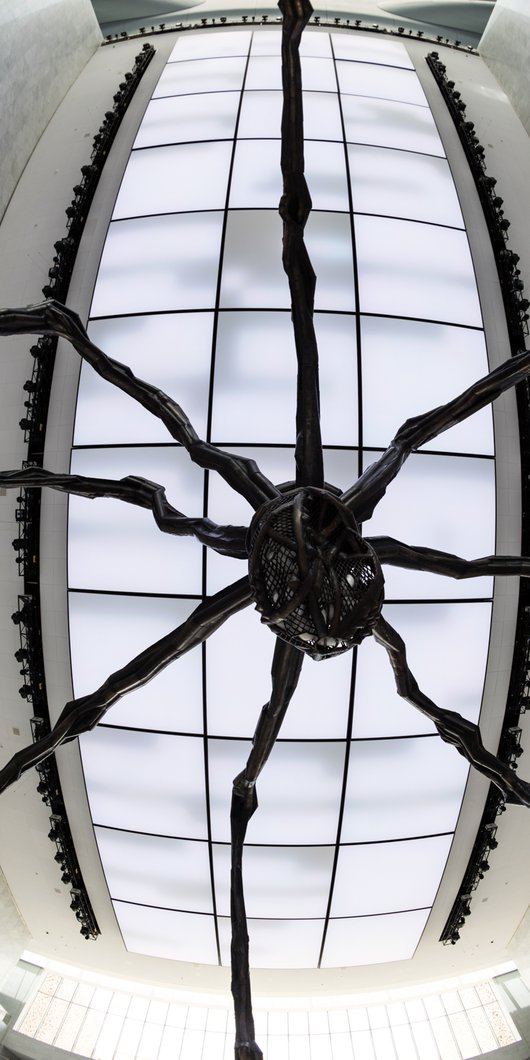 A close-up shot from under the sculpture showing the detailed bronze and stainless steel work around the Maman's body