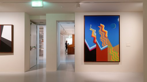 View of a gallery corner, looking through to different spaces, with two artworks hanging in view.