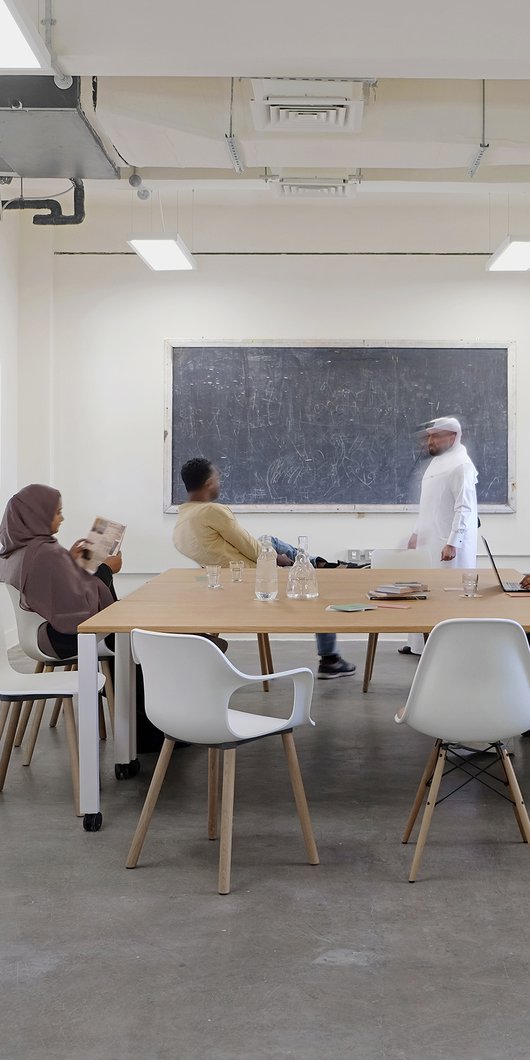 A small meeting room, with a central table and chairs with several people.