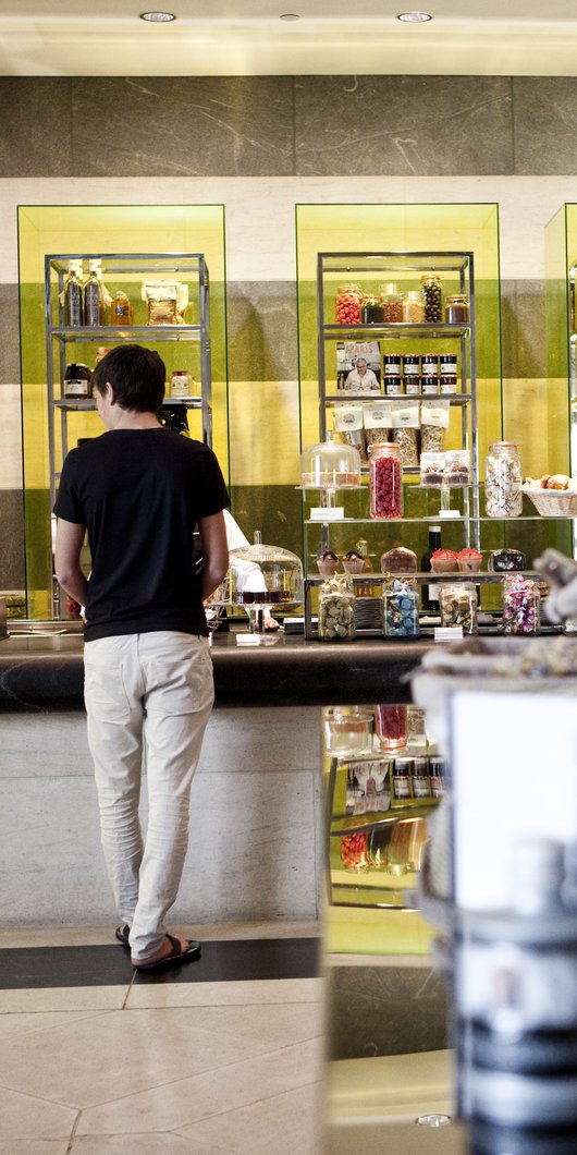 A man standing at a food counter with colourful food and beverages displayed along the rear wall