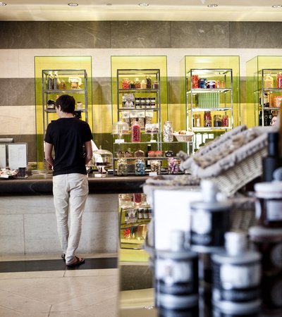 A man standing at a food counter with colourful food and beverages displayed along the rear wall